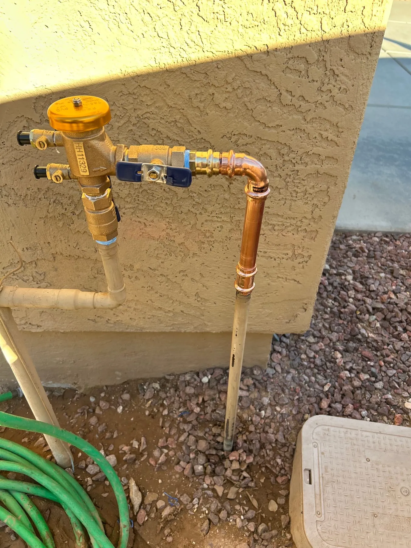 Brass backflow preventer and copper supply line installed against a stucco wall