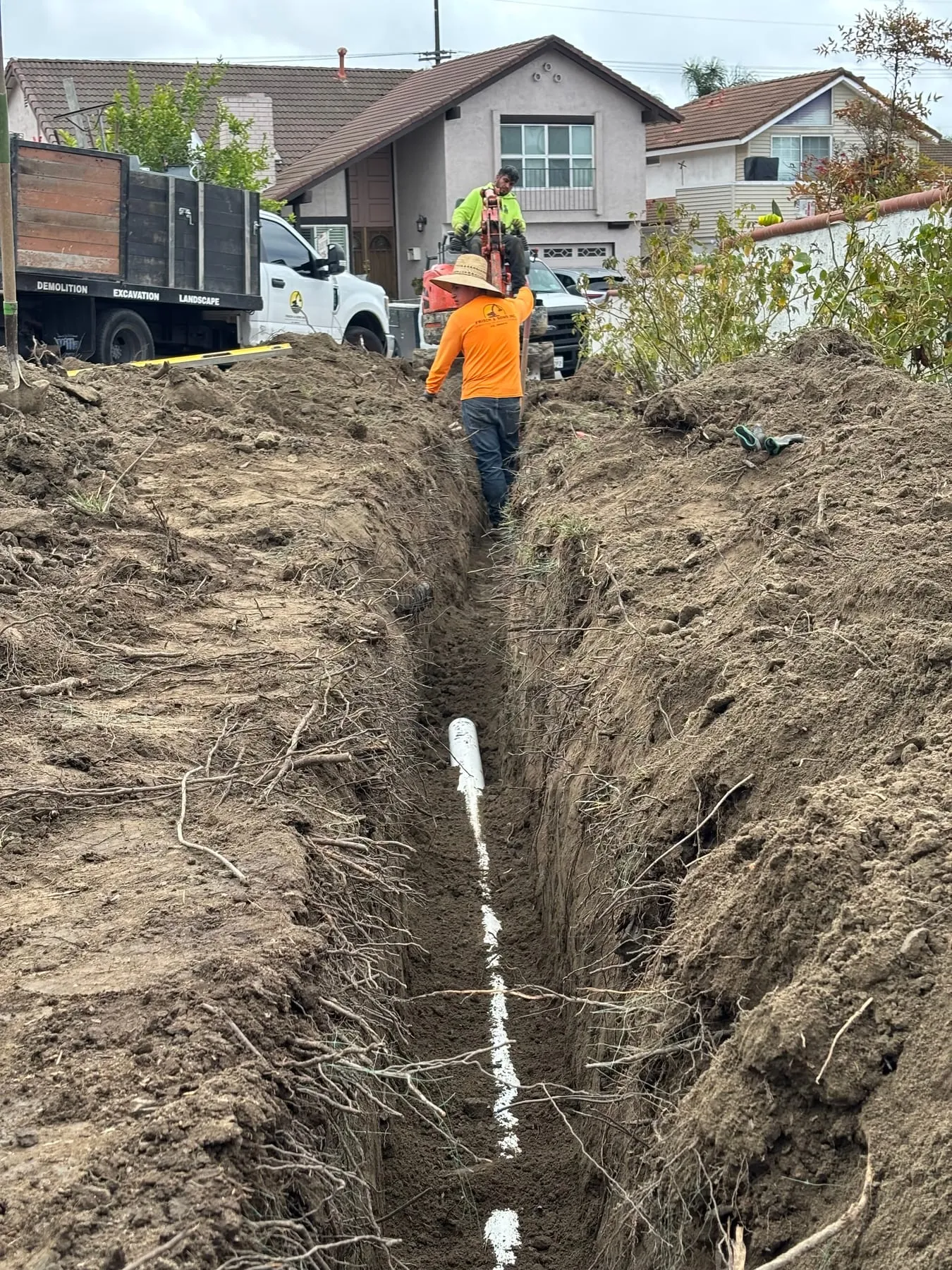 Crew member in an open trench with a white PVC irrigation line laid along the bottom