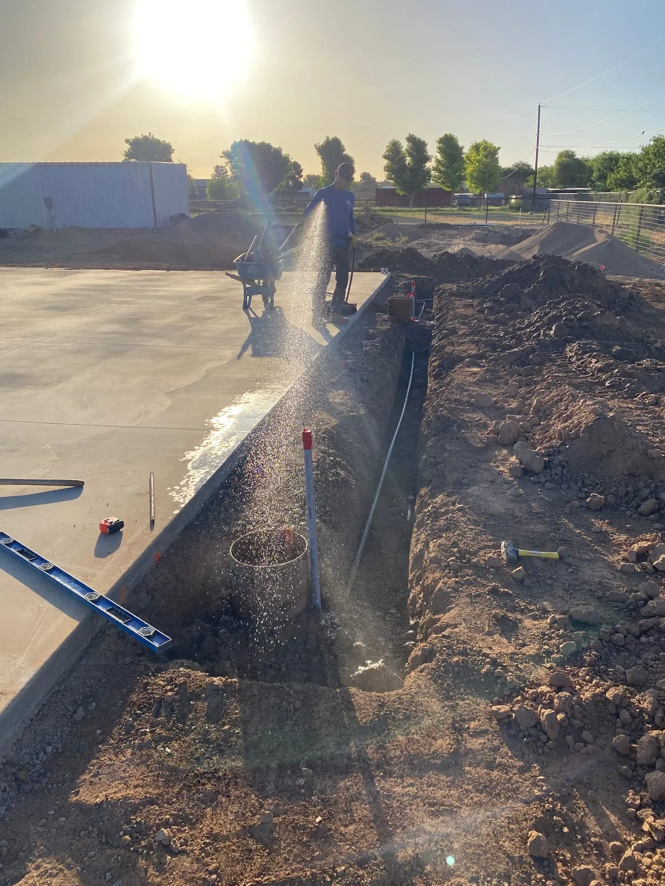 Sprinkler spraying beside a newly dug irrigation trench next to a concrete slab